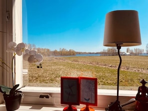 A window with a view of a lake, a lamp, and two framed pictures. - 5 Person Holiday Home in Alvesta (Alvesta)
