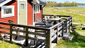 Eine rote Holzhütte mit einer Terrasse, einem Tisch und Stühlen mit Blick auf einen See.