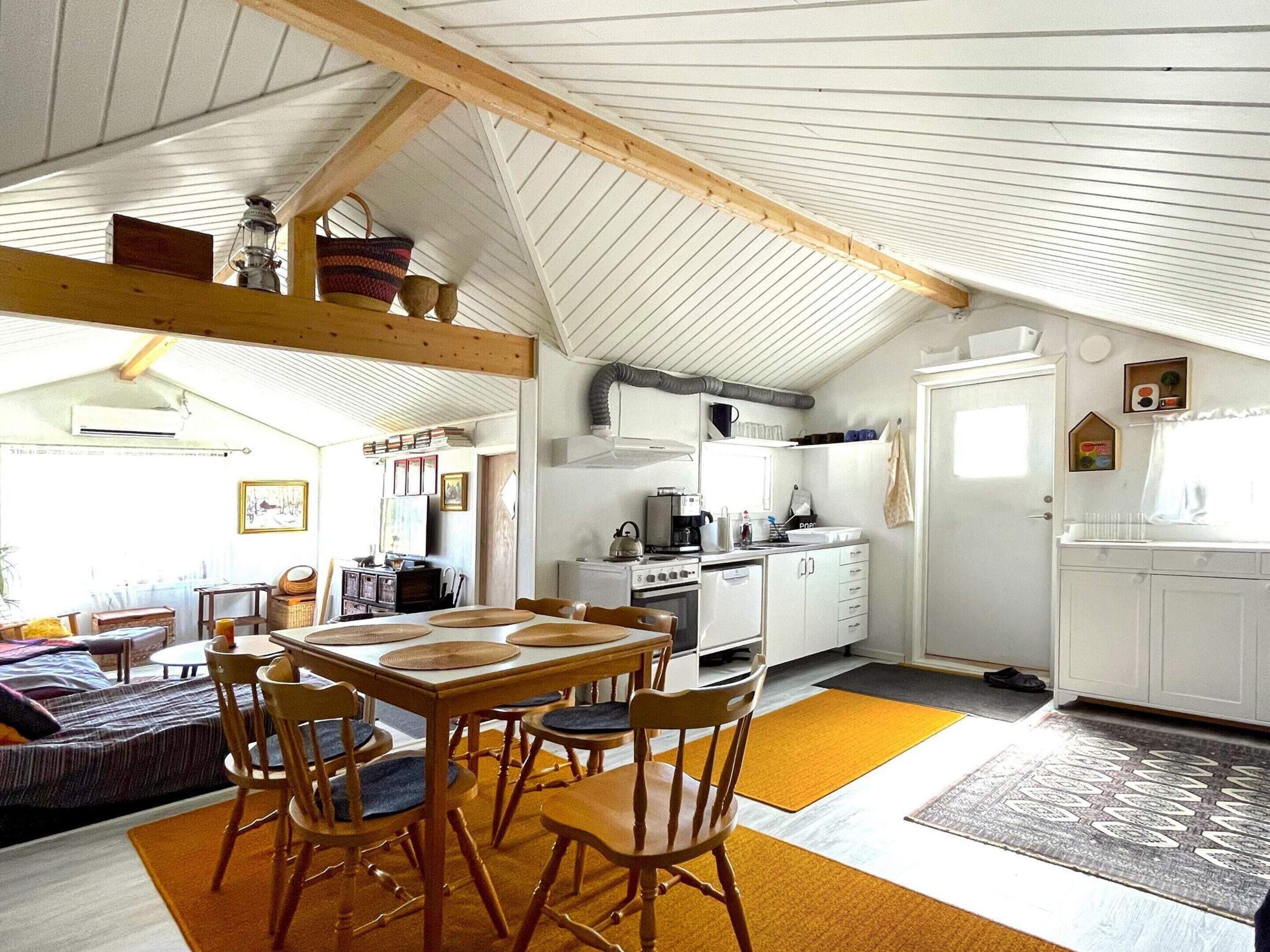 A cozy kitchen with wooden beams, a dining area with a table and chairs, and a small kitchenette.