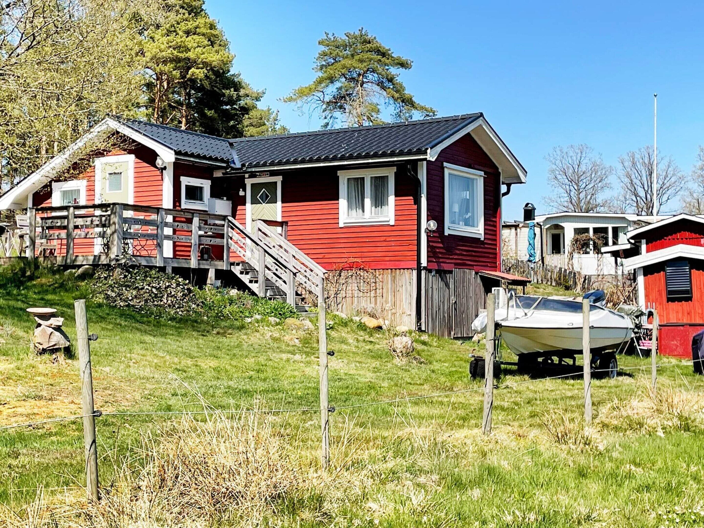A red house with a staircase leading to a deck, a boat in the yard, and a fence.