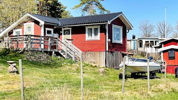 Una casa roja con una escalera que lleva a una terraza, un barco en el jardín y una valla.