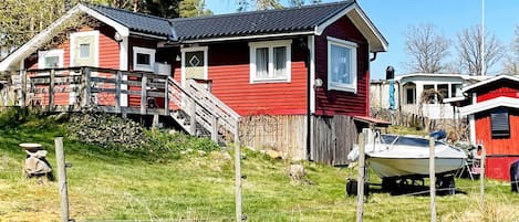 A red house with a staircase leading to a deck, a boat in the yard, and a fence.