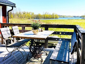 Una terraza de madera con una mesa, sillas, una planta en maceta y vistas a un lago.
