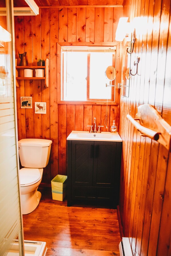 Ein kleines Badezimmer in einer Holzhütte mit Toilette, Waschbecken und Fenster.