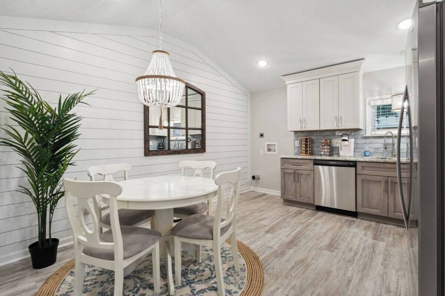 Una cocina moderna con armarios blancos, un refrigerador de acero inoxidable y una zona de comedor con una mesa redonda y sillas.