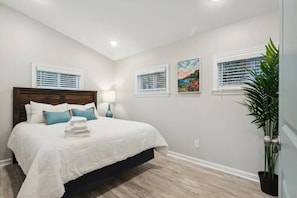 A bedroom with a bed, bedside tables, a nightstand, a potted plant, and artwork on the walls. - Sunnyside Inn Back Cottage (Hampton)