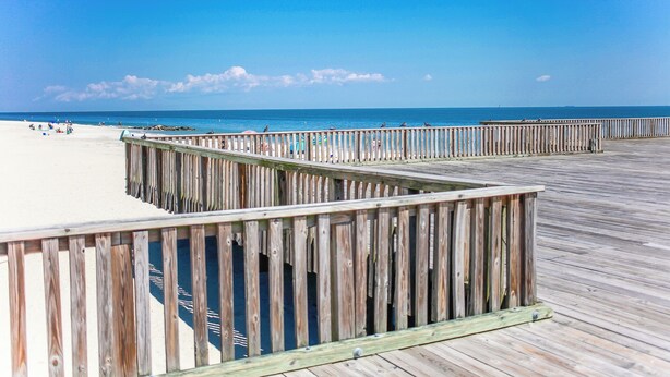A wooden boardwalk leading to a sandy beach with clear skies.