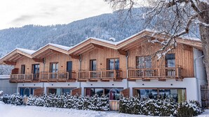 A wooden chalet with multiple balconies, large windows, and a snowy landscape in the background. - Large Chalet With Carmine and Wellness Area (Reith bei Kitzbuehel)
