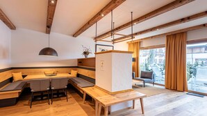 A modern interior with a wooden bench seating area, a central table, and a view through large windows. - Large Chalet With Carmine and Wellness Area (Reith bei Kitzbuehel)