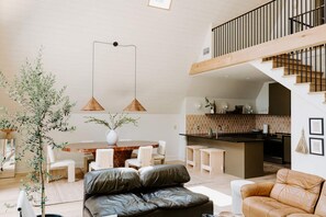 A spacious living area with a dining table, leather sofas, and a kitchen with a black countertop. - Stayframe: a designer getaway with mountain views (Monteagle)