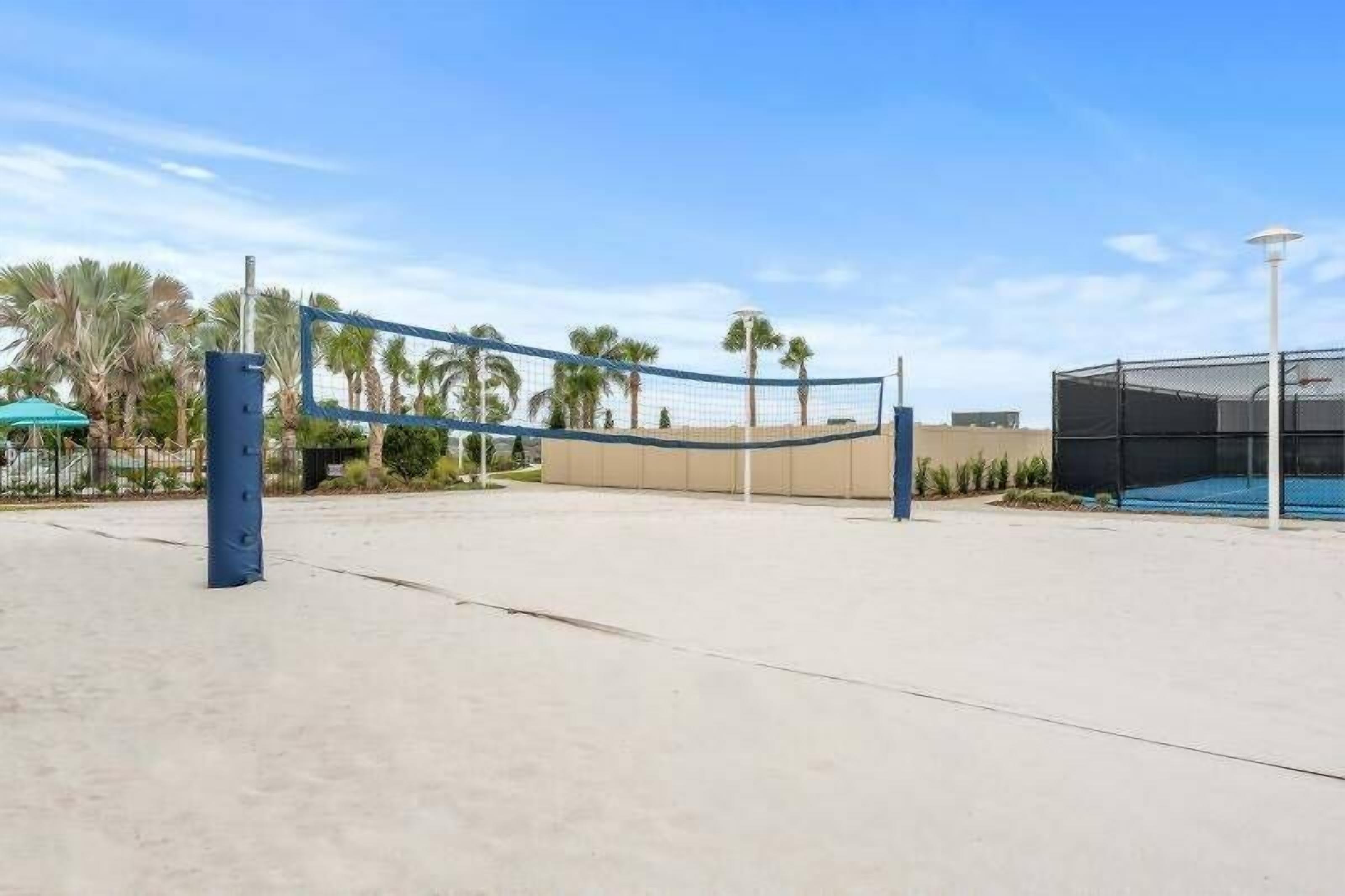 An outdoor volleyball court with a net, palm trees, and a building in the background.