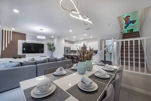 Eine moderne Küche mit Essbereich, einer Treppe und einem Wohnzimmer mit Sofa und Fernseher.