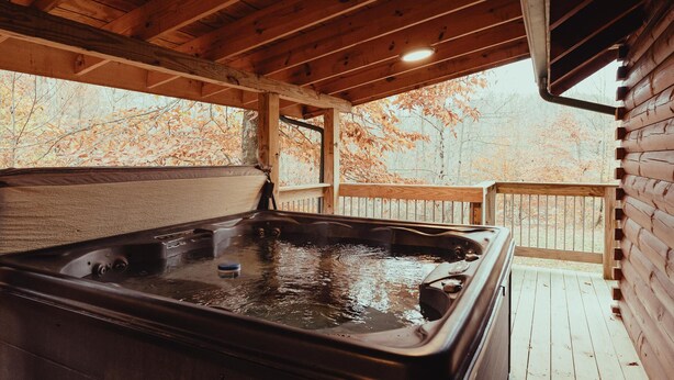 Una terraza de madera con un jacuzzi, barandillas de madera y vistas a árboles.