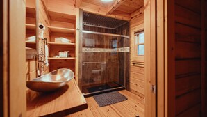 Interior de una cabaña de madera con ducha de vidrio, lavabo de madera y un perchero para toallas.