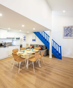 A modern kitchen with white cabinets, a microwave, and a dining area with a wooden table and wicker chairs.