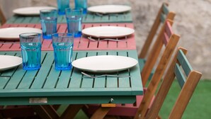 Une table dressée avec des assiettes et des verres bleus, des chaises en bois et un mur de pierres en arrière-plan.
