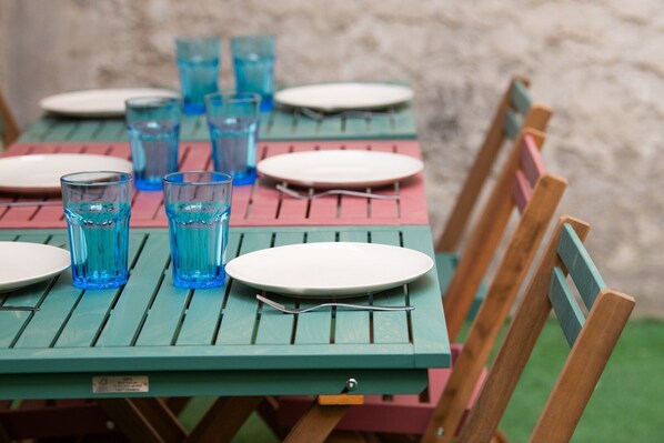 A table set with plates and blue glasses, wooden chairs, and a stone wall background.