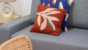 Un canapé gris agrémenté d’un coussin coloré et d’un tableau abstrait encadré accroché au mur.