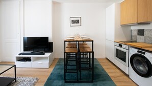 A compact living space with a TV, a small dining table, a washing machine, and a kitchen area.