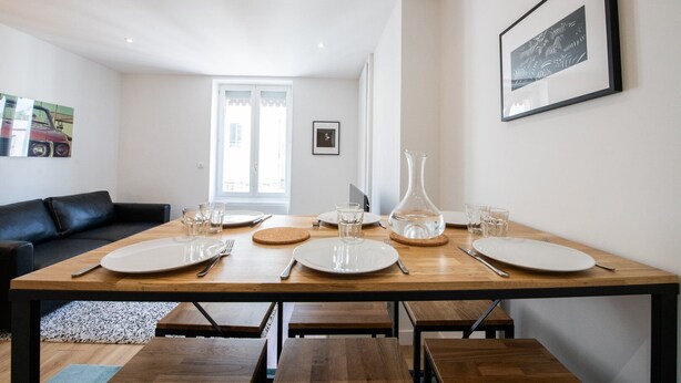 A dining area with a wooden table set for four, a black leather couch, and a framed picture on the wall.