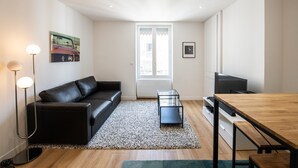 A modern living room with a black leather sofa, a glass coffee table, a wooden dining table, and a TV.