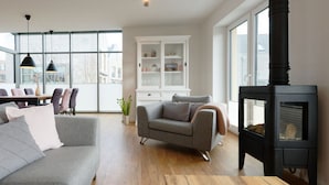 A modern living room with a sofa, a wooden coffee table, a fireplace, and a dining area with chairs and a table. - Holiday Home Traumhuus (Varel)