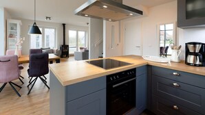 A modern kitchen with a central island, built-in oven, and a large range hood. - Holiday Home Traumhuus (Varel)