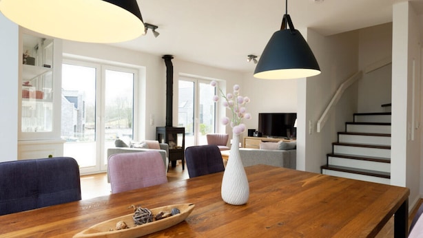 A modern living room with a wooden dining table, two pendant lights, a white vase, and a small decorative boat. - Holiday Home Traumhuus (Varel)