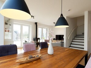 A modern living room with a wooden dining table, two pendant lights, a white vase, and a small decorative boat. - Holiday Home Traumhuus (Varel)