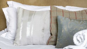 Un lit avec une tête de lit beige, des oreillers blancs à motifs et un couvre-lit blanc.