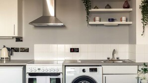 Une cuisine moderne avec des meubles blancs, une hotte en acier inoxydable, un four encastré, un lave-linge et un évier.