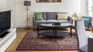 A modern living room with a grey sofa, a round coffee table, a floor lamp, and a colorful abstract painting on the wall. - Balcony South Kensington Luxury 2 bed Apartment (London)