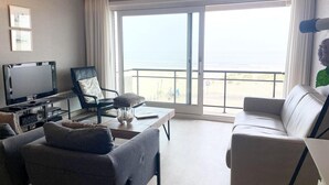 A living room with a TV, two sofas, a coffee table, and a balcony with a view of the sea. - Apartment in Nieuwpoort by the Beach (Nieuwpoort)