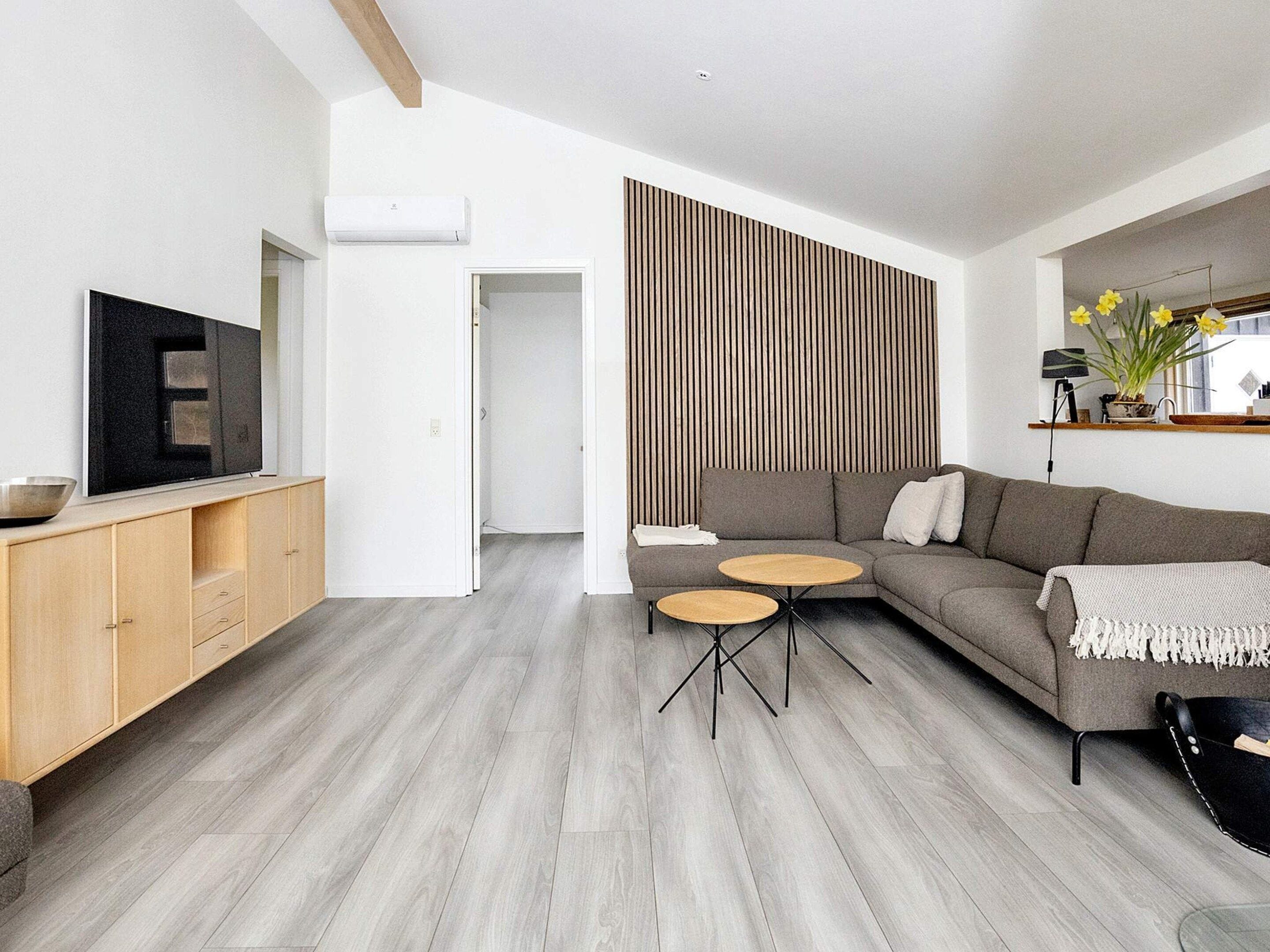 Una sala de estar moderna con un sofá modular, un televisor de pantalla plana y un comedor con mesa y sillas de madera.