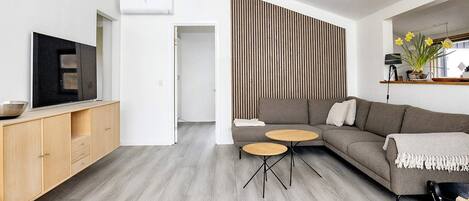Una sala de estar moderna con un sofá modular, un televisor de pantalla plana y un comedor con mesa y sillas de madera.