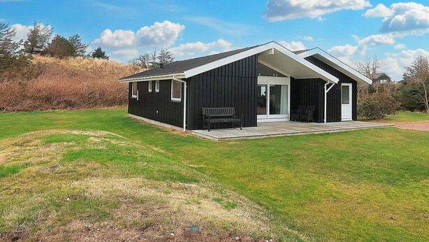 Een modern zwart gebouw met terras, omringd door gras en bomen.