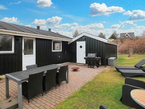 A patio area with a table and chairs, a grill, and a shed. - 4 Star Holiday Home in Blokhus (Blokhus)