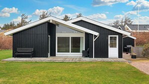 Een modern huis met twee verdiepingen, een donkere gevel, grote schuifpuien en een klein terras.
