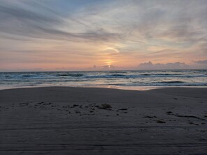 Una playa con atardecer, olas y huellas.