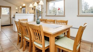 Een eetgedeelte met een houten tafel en stoelen, een vaas met takken en hanglampen.