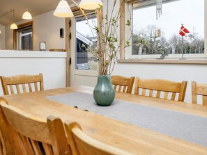 Un comedor con mesa de madera, sillas, un jarrón con ramas y una ventana con una bandera.
