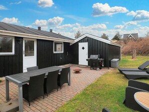 A patio area with a table and chairs, a grill, and a small shed. - 4 Star Holiday Home in Blokhus (Blokhus)