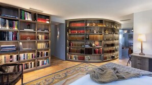 Una habitación amplia con una gran librería curvada llena de libros, una cama cómoda con una colcha estampada y un escritorio pequeño con una lámpara.