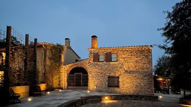 Un edificio de piedra con un patio empedrado, una verja de metal y un banco.