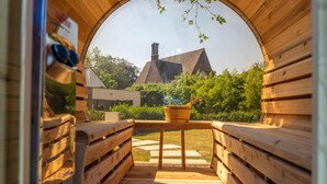A wooden sauna with benches and a table, a view of a house and trees in the background. - Luxury Villa With Pool & Sauna Kortrijk (Kortrijk)