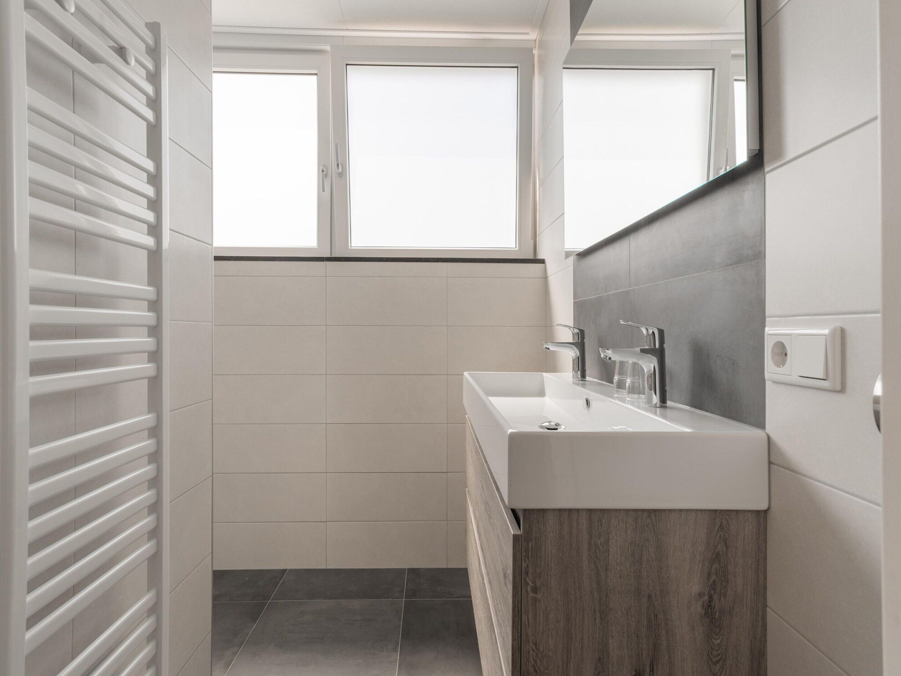 Een moderne badkamer met een wit wastafelmeubel, een spiegel en een raam.
