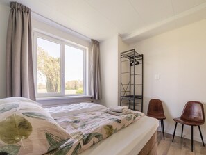A bedroom with a bed, a window with curtains, a metal shelf, and two chairs. - Cozy Holiday Home in Oploo Near Forest (Oploo)