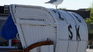 Une chaise de plage avec un dossier en osier tressé et un accoudoir en bois.