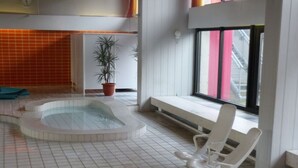 Une piscine intérieure moderne, dotée d’un jacuzzi, d’une plante en pot et d’un banc placé près d’une fenêtre offrant une vue sur un bâtiment.
