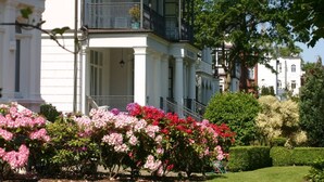A white building with a balcony and a garden with pink flowers. - Sandpiper in Haus Strandburg Binz (Binz)